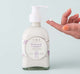 A hand next to a bottle of Buttermilk Lavender Steeped Milk Lotion for body, infused with coconut milk and organic lavender flowers from Farmhouse Fresh.
