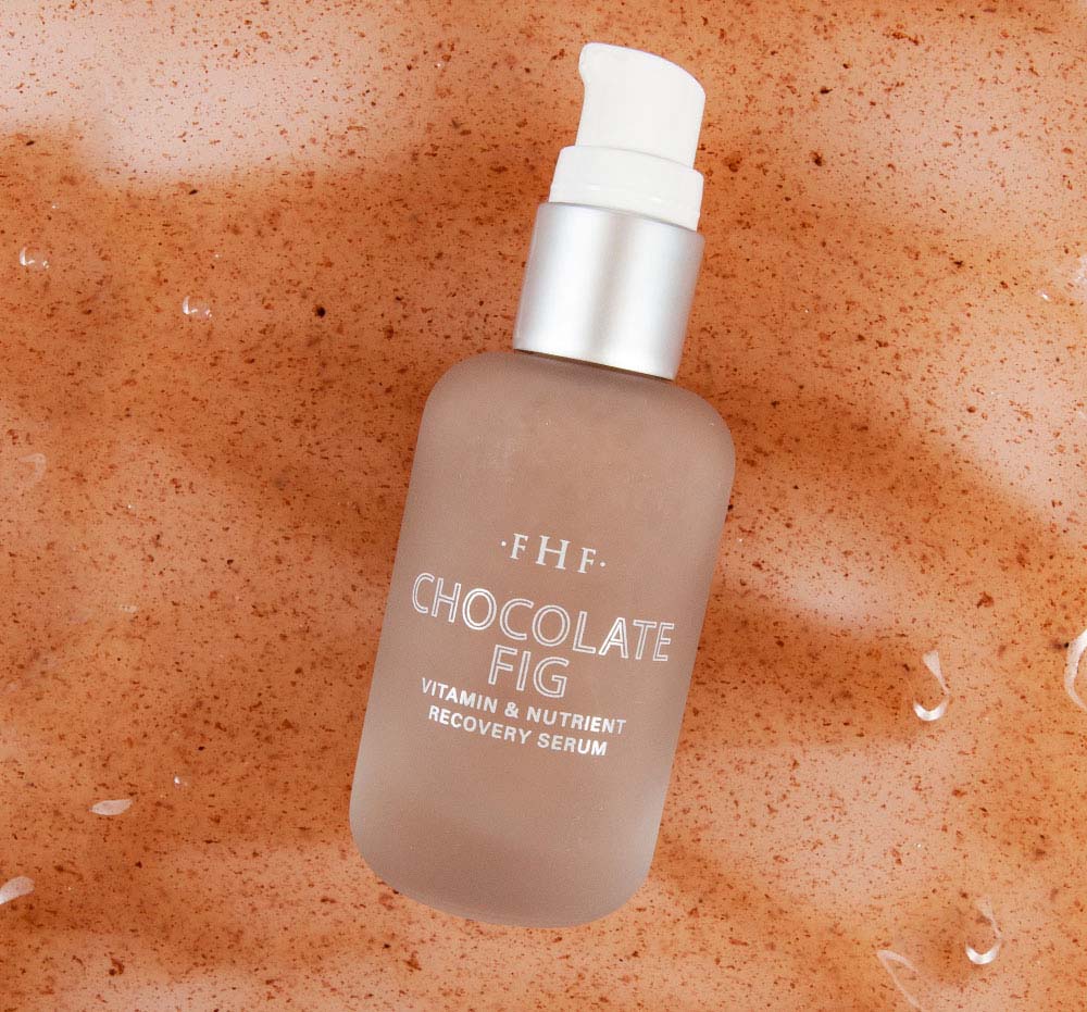 A bottle of FarmHouse Fresh Chocolate Fig Vitamin Recovery Serum on top of texture swatch that highlights the natural ingredients of this skincare product.