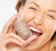 A smiling woman is holding a bottle of FarmHouse Fresh Chocolate Fig Vitamin Recovery Serum, showing her moisturized and healthy-looking skin.