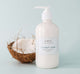 A coconut next to a bottle of Farmhouse Fresh Coconut Cream Shea Butter body lotion that provides nourishment and moisturization for dry skin.