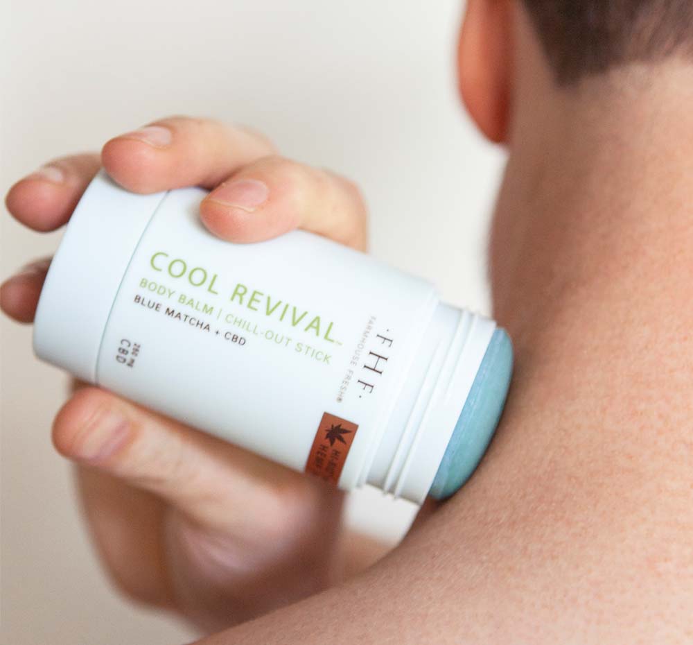 A man is applying Cool Revival Body Balm with CBD by FarmHouse Fresh on his neck to ease muscle tension and cool down his skin.