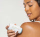 A woman is applying Cool Revival Body Balm with CBD by FarmHouse Fresh on her shoulder to cool her skin after the sun.