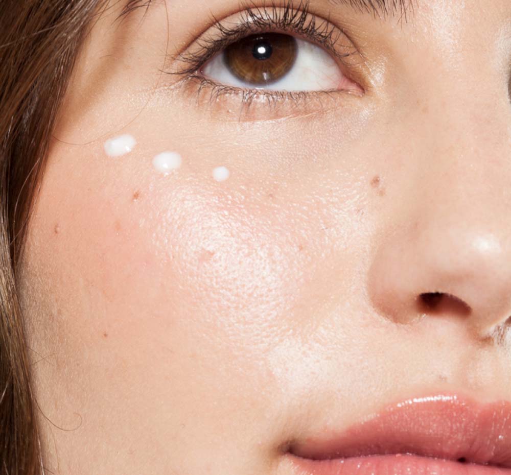 A close up of a woman's face with Farmhouse Fresh Crow Catcher serum applied to her eye area, targeting wrinkles.