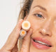 A woman is holding a tube of FarmHouse Fresh Orange Mood Fruit Lip balm that nourishes lips with a hint of color.
