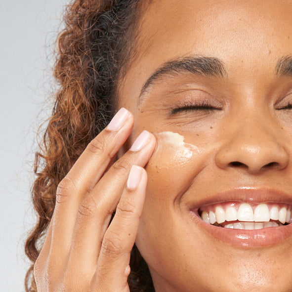 A woman is applying FarmHouse Fresh Stunning Returns Ultra-Rich Bakuchiol Butter on her face to deeply hydrate and soften her skin.