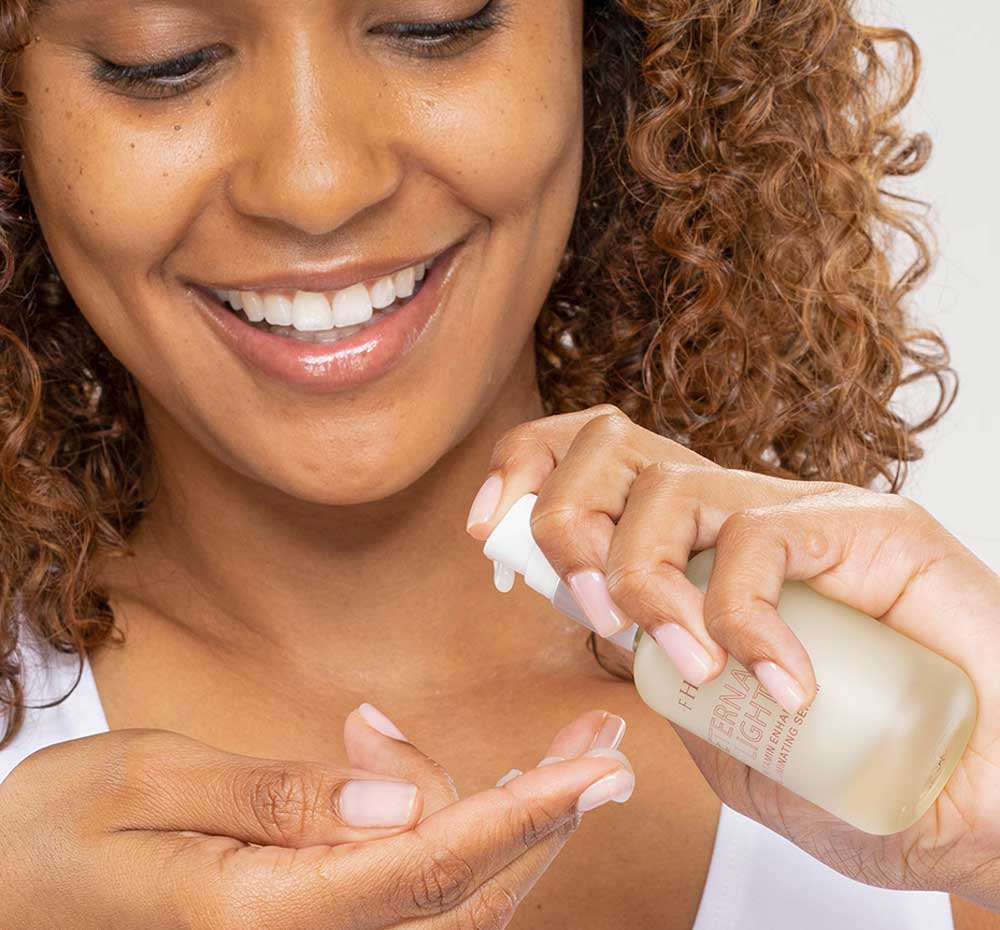 A woman is holding a bottle of FarmHouse Fresh Eternal Light Face Serum with vitamin C, ready to apply it to her face to make skin look radiant.