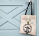 A FarmHouse Fresh® canvas bag with patches featuring an image of a goat hanging on the door.
