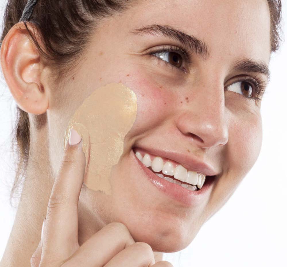 A woman is applying Mighty Tighty Turmeric & Banana Mask by FarmHouse Fresh on her face to tighten and smoothen her skin.