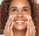 A woman is applying FarmHouse Fresh Fields of Green Organic Matcha Ultra-Soothing Moisturizer on her face to hydrate skin and reduce redness.