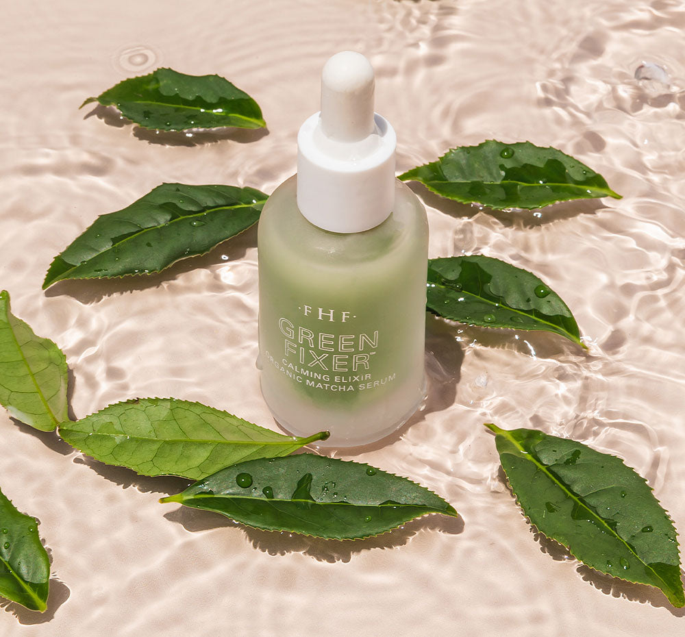 A bottle of FarmHouse Fresh Green Fixer Calming Elixir Organic Matcha Face Serum standing in the water, surrounded by leaves that represent the moisturizing properties and natural ingredients of this skincare product.