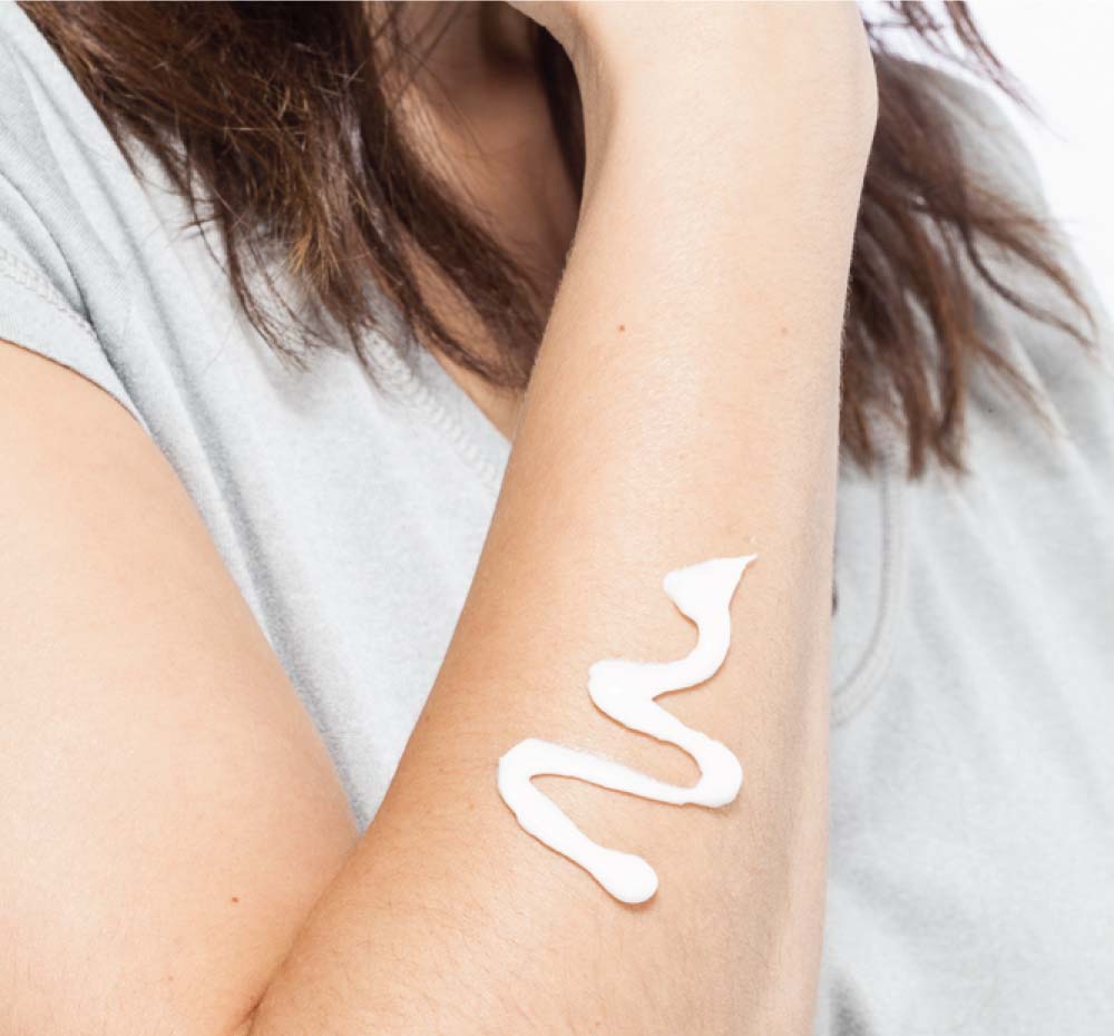 A woman’s arm with a smear of FarmHouse Fresh Harvest Green Shea Butter on it that shows the rich texture of this body moisturizer.