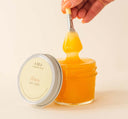 A hand dipping a brush into an open jar of Honey Heel Glaze by FarmHouse Fresh, made to transform cracked heels.