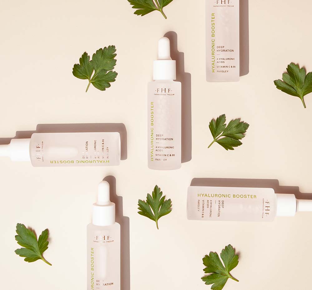 Bottles of FarmHouse Fresh Hyaluronic Boosters next to parsley leaves that represent the natural antioxidant-rich ingredients.