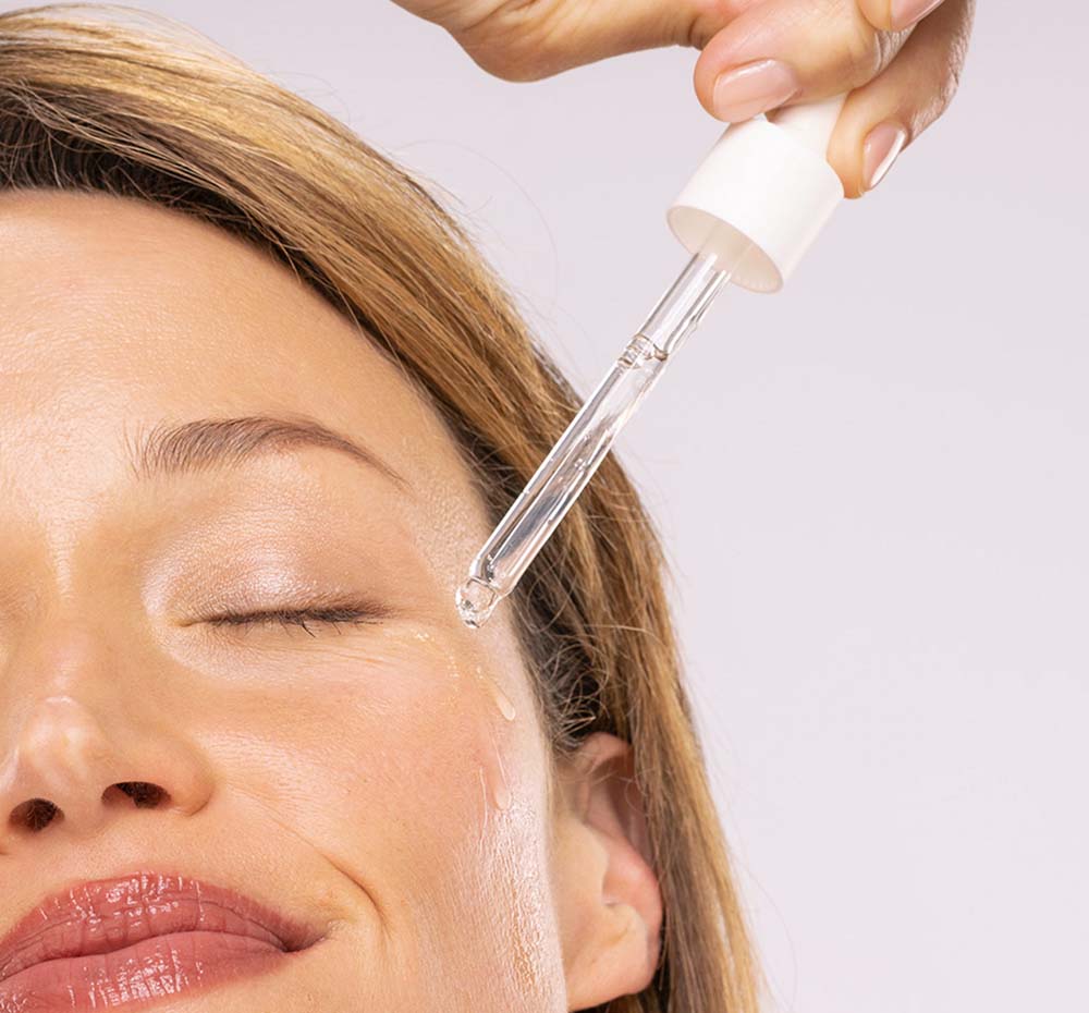 A woman is applying FarmHouse Fresh Hyaluronic Booster on her face to bring a visibly refined, healthy, calmed appearance to her skin.