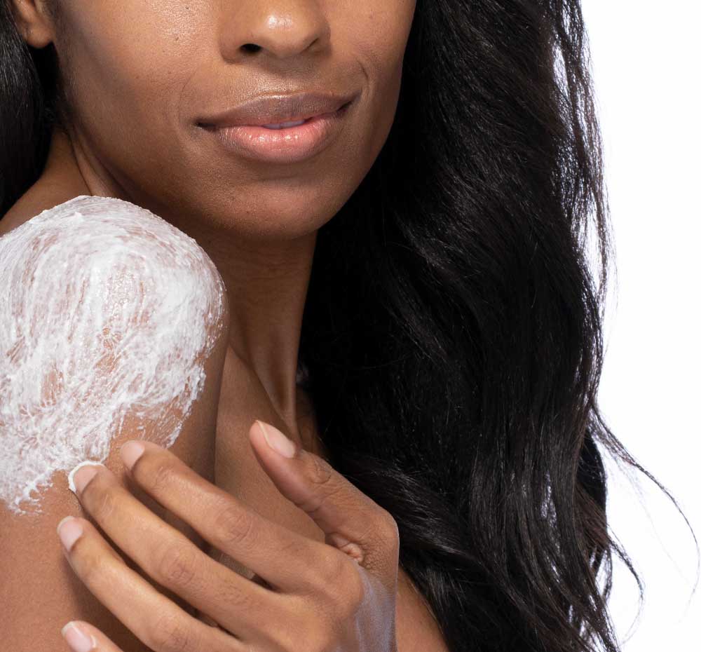 A woman is applying FarmHouse Fresh Lime So Fine Foaming Body scrub onto her shoulder to cleanse and exfoliate skin.