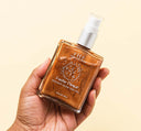 A hand holding a bottle of FarmHouse Fresh Lustre Drench Instant Glow Dry Oil with all-natural lemon-cream scent.