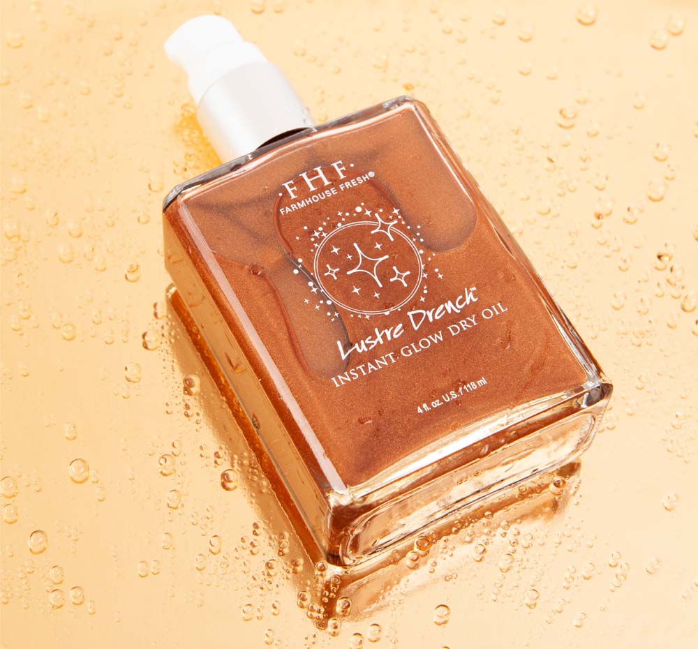 A bottle of FarmHouse Fresh’s nourishing Lustre Drench Instant Glow Dry Oil on top of water beads, showing the product’s moisturizing properties.