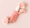 A bottle of FarmHouse Fresh Lustre Rose Serum-in-Oil made with organic rose hydrosol next to rose flowers.
