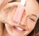 A woman is holding a bottle of FarmHouse Fresh Lustre Rose Serum-in-Oil that hydrates and brightens skin.