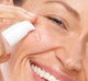 A woman is applying FarmHouse Fresh Lustre Rose Serum-in-Oil on her face to soften and moisturize her skin.
