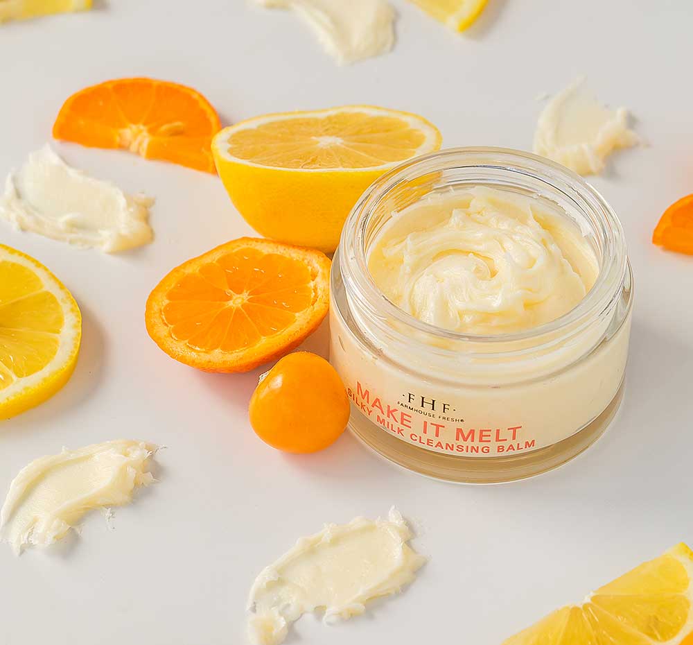 A jar of FarmHouse Fresh Make It Melt Silky Milk Cleansing Balm next to oranges, demonstrating the natural ingredients that reduce the visible look of redness, itchiness, and uneven skin tone.