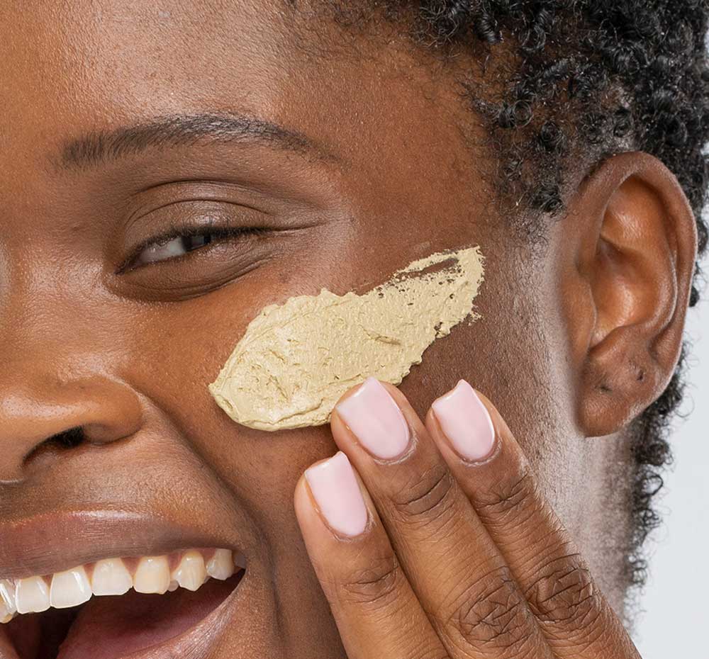 A woman is applying Matcha Purity Purification Mask by FarmHouse Fresh on her face to calm, hydrate and smooth her sensitive skin.