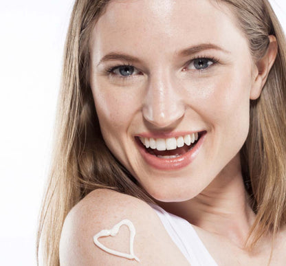 A woman with FarmHouse Fresh Steeped Milk Lotion for Hands in shape of a heart on her shoulder is smiling, hinting to the pleasant passion fruit scent of the product.