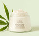 A jar of Mellow Moon Dip Body Mousse by FarmHouse Fresh next to a hemp leaf that represents full spectrum hemp oil with CBD as one of the main ingredients in this skincare product.