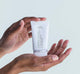Hands holding a tube of FarmHouse Fresh Midnight Clearing Night Lotion that clears acne without over-drying skin.