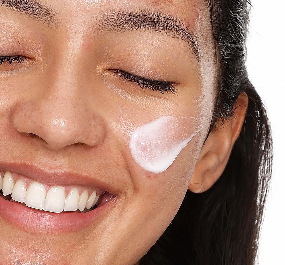 A woman is applying FarmHouse Fresh Midnight Clearing Night Lotion acne treatment to her face to clear and soften her skin.