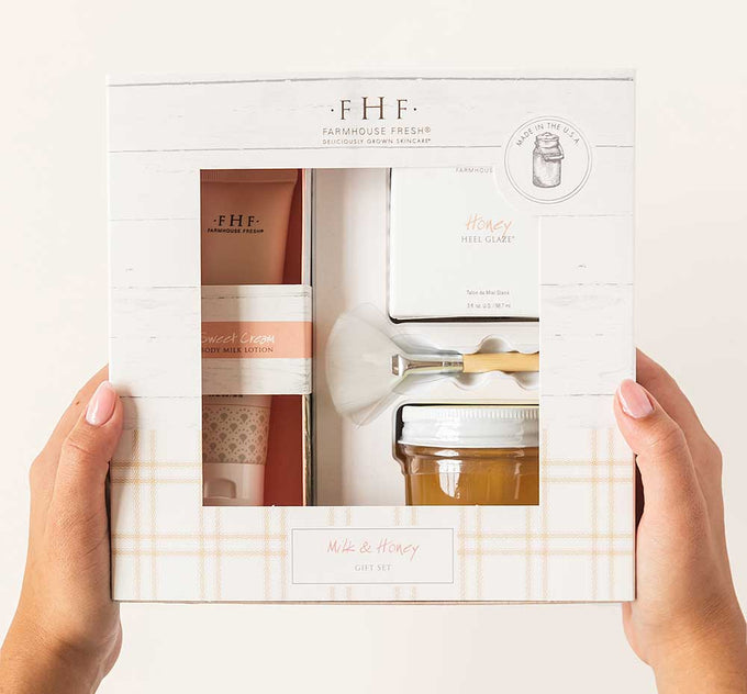 Hands holding a box of Milk & Honey Deluxe Boxed Gift Set by FarmHouse Fresh that includes a travel-size Sweet Cream body milk lotion and Honey Heel Glaze serum for dry, cracked feet.