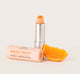 A tube of all-natural FarmHouse Fresh Orange Mood Fruit Lip Therapy balm next to a wedge of orange.