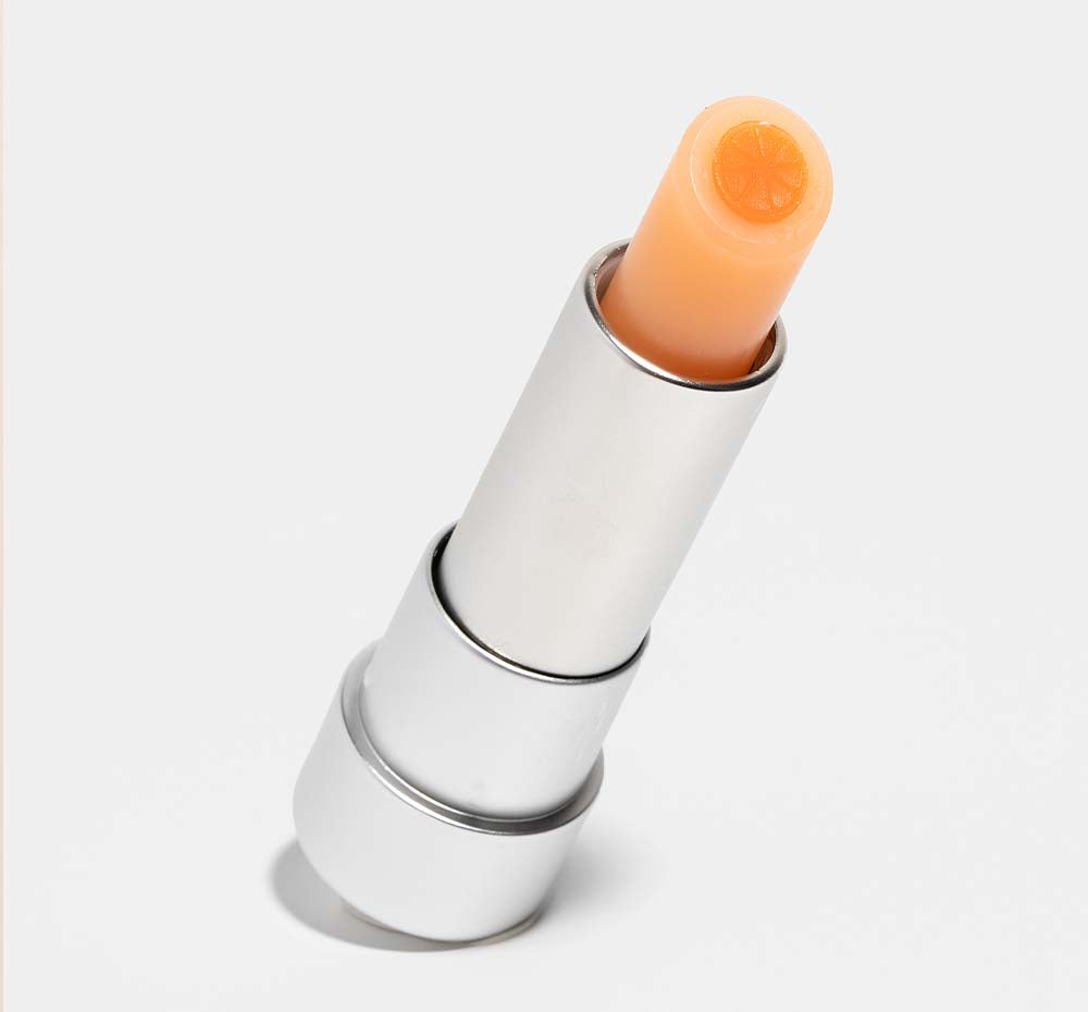 An open tube of FarmHouse Fresh Orange Mood Fruit tinted lip balm made with natural extracts and vitamins that nourish and soothe dry lips.