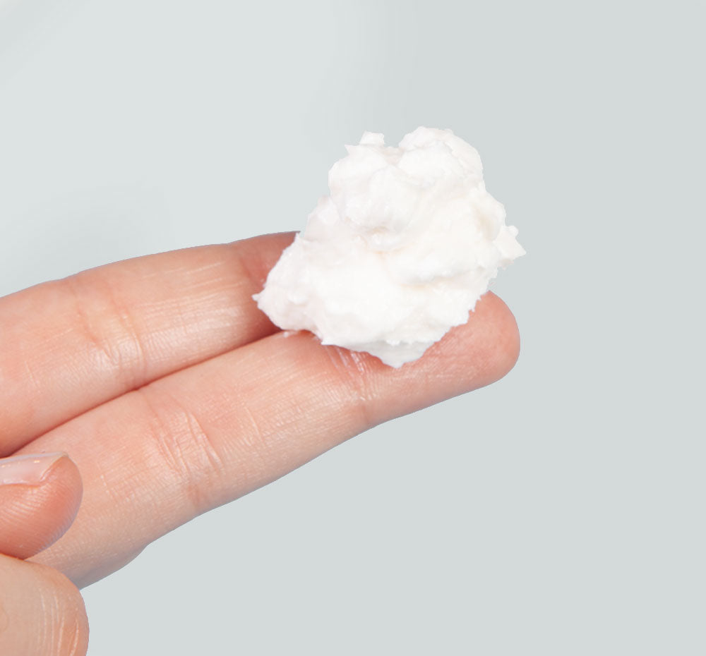 A hand holding a dollop of Sugar Moon Dip Body cream by FarmHouse Fresh showing the whipped, light texture of the body mousse.