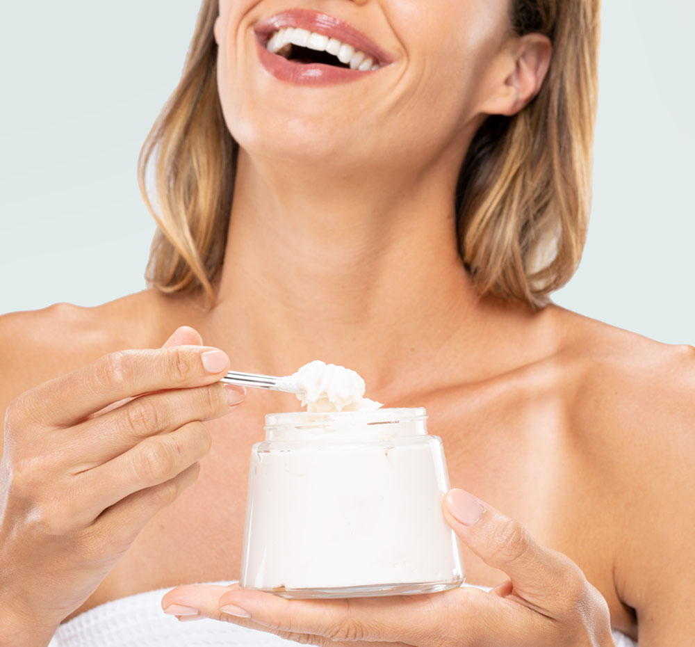 A woman is holding a jar of FarmHouse Fresh Sugar Moon Dip Body Mousse and an applicator wand, ready to nourish and soften her skin.