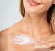 A woman is applying FarmHouse Fresh Unscented Moon Dip Body Mousse on her décolleté area to nourish and soften her skin.