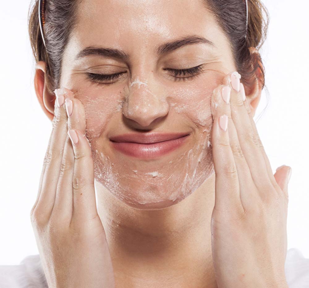 A woman is exfoliating her face with FarmHouse Fresh One Fine Day Face scrub and cleanser made with shea butter to nourish skin.