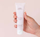 A hand holding a tube of FarmHouse Fresh Pink Moon Shea Butter hand cream that leaves skin hydrated and soft.