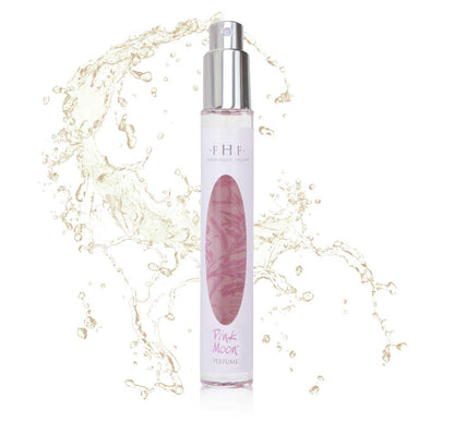 A bottle of Farmhouse Fresh perfume with a splash of water, exuding the soft licorice blossom, powder and spun sugar scent of Pink Moon Travel Spray.