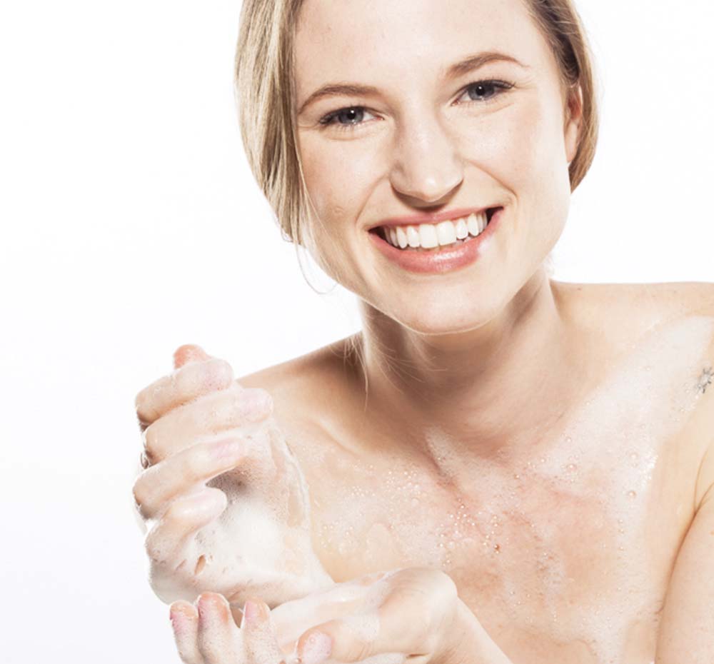 A woman is washing her body with FarmHouse Fresh Rainbow Road Soothing Body Wash scented with a light, uplifting blend of coconut and Bartlett pear.