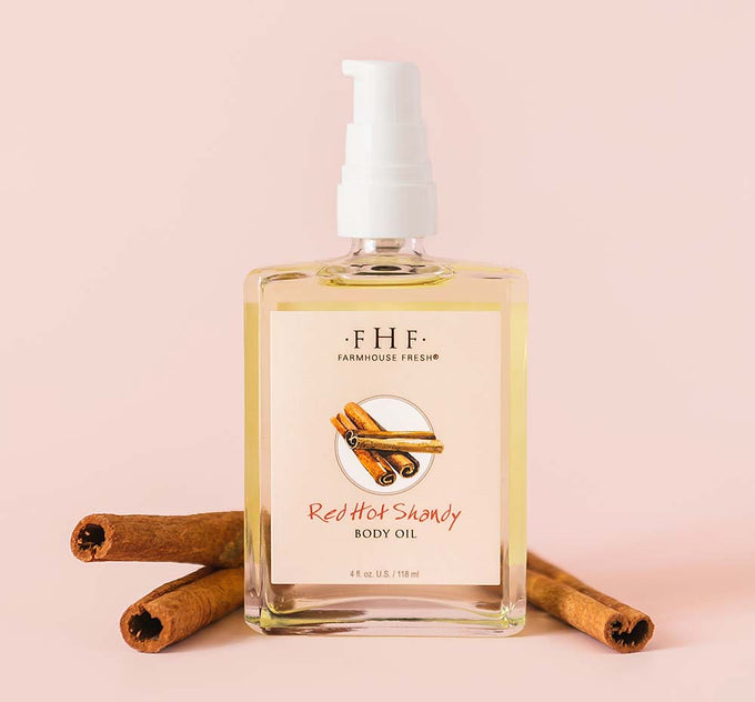 A bottle of Farmhouse Fresh Red Hot Shandy Body Oil next to cinnamon sticks signifying its warm and spicy gingerbread scent.