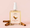 A bottle of Farmhouse Fresh Red Hot Shandy Body Oil next to cinnamon sticks signifying its warm and spicy gingerbread scent.