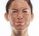 A woman with Farmhouse Fresh Sanded Ground exfoliating mask on her face, the perfect skincare product to clear skin and reduce the appearance of pores.