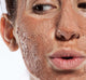 A woman with Farmhouse Fresh Sanded Ground exfoliating face Mask on her face, a staple skincare product to clear acne.