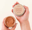 Hands holding a jar of Farmhouse Fresh Sanded Ground Clarifying Mud Exfoliation Mask for acneic, blemish-prone and oily skin.