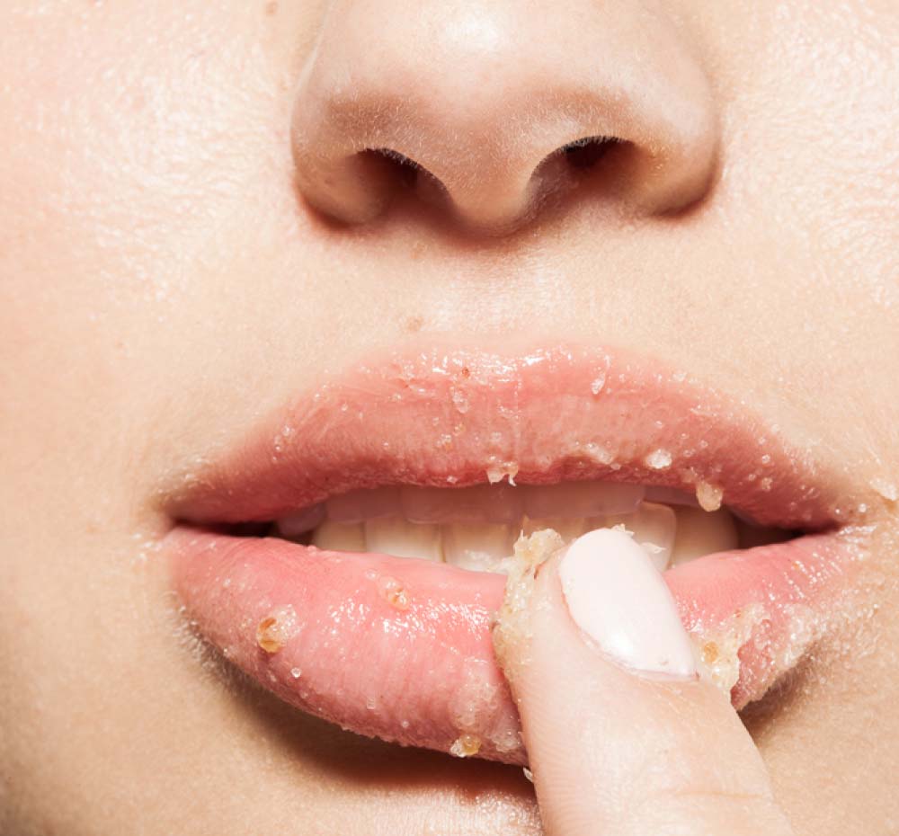 A woman is exfoliating her lips with FarmHouse Fresh Strawberry Wine lip polish made with natural, locally sourced ingredients.