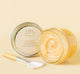 A jar of FarmHouse Fresh Sunflower Honey-Butter next to a brush that helps apply this serum to skin to lock in moisture.