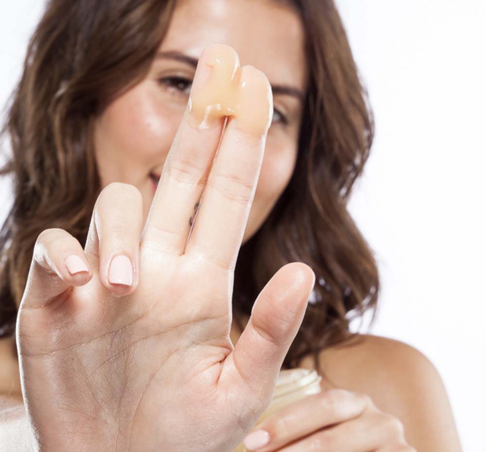 A woman is holding FarmHouse Fresh’s Organic Sunflower Honey-Butter on her fingers, ready to deeply moisturize her dry skin.