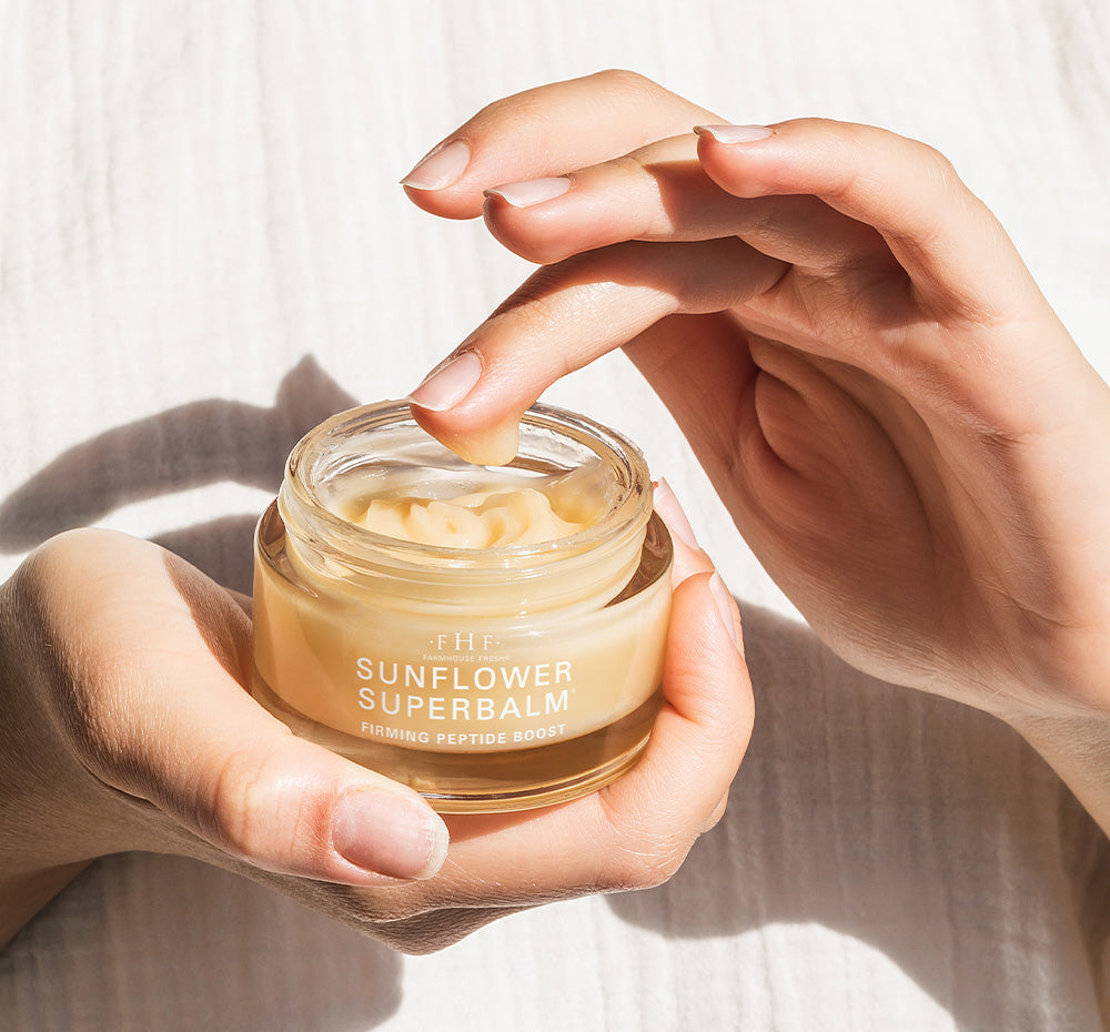 Woman’s hands holding a jar of FarmHouse Fresh Sunflower Superbalm Firming Peptide Boost face balm made with nourishing golden organic sunflower seed oil.