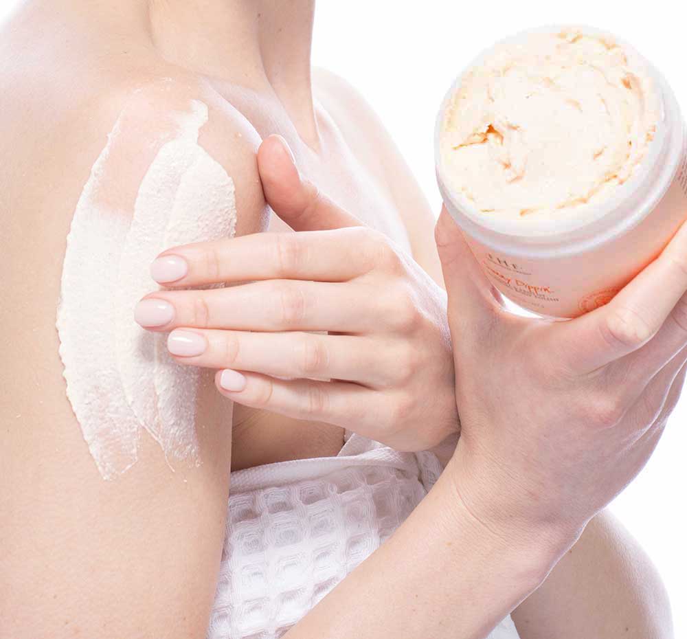 A woman is applying FarmHouse Fresh Sunny Dippin’ Foaming Body scrub onto her shoulder to cleanse and exfoliate skin.